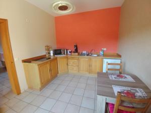uma cozinha com paredes cor de laranja, armários de madeira e uma mesa em Gîte du Vieux Chemin em Durbuy