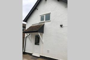 a white house with a black roof and a door at Charming just renovated 2 bed cottage in the centre of village in Hartford