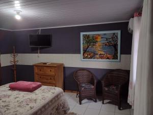 a bedroom with a bed and two chairs and a tv at Rancho Velho Tropeiro in São Francisco do Sul