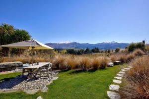 einen Picknicktisch mit Sonnenschirm im Garten in der Unterkunft Hawkridge Chalet - Honeymooners Chalet in Arrowtown