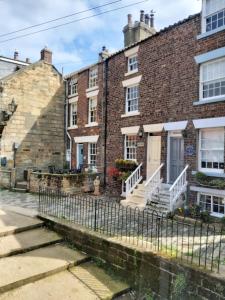 an old brick building with a fence in front of it at Dunsley Cottage in Staithes