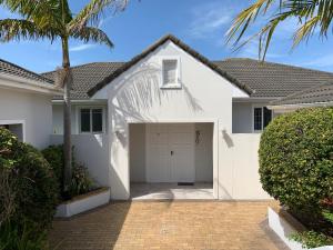 a white house with a garage and a palm tree at 56 Robberg Road Plettenberg Bay in Plettenberg Bay