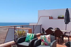 einen Balkon mit Stühlen, Tischen und einem Sonnenschirm in der Unterkunft Casa Las Olas in Cotillo