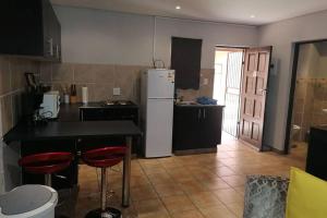 cocina con nevera blanca y taburetes rojos en BEAUTIFUL APARTM B10 SITUATED IN BAINS GAME LODGE, en Bloemfontein