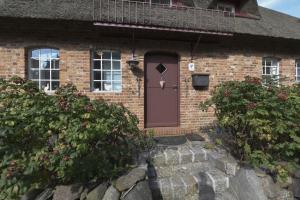 ein Backsteinhaus mit brauner Tür und einigen Büschen in der Unterkunft Haus Hahnenhof Whg 08 in Wrixum