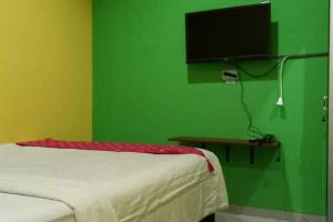 een slaapkamer met een groene muur met een bed en een televisie bij RedDoorz near Bandara Adi Soemarmo Solo in Tjolomadu