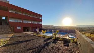 a red building with a swimming pool and a sunset at Pousada Morada dos Pássaros in Capitólio