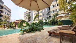 una piscina con 2 bancos y una sombrilla en Portal das Palmeiras 2, en Ubatuba