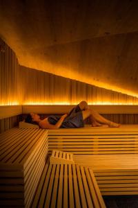 a woman laying in a sauna with a man laying on it at Linder Cycling Hotel in Selva di Val Gardena