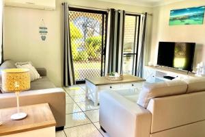 a living room with a couch and a tv at WHISPERING PALMS in Bongaree