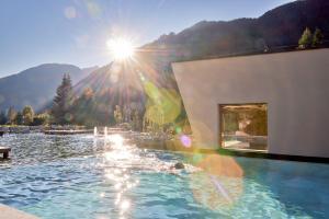 a swimming pool with the sun shining on the water at FONTIS luxury spa lodge in Santa Maddalena in Casies Valbassa
