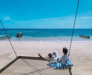 a man sitting on a hammock with a laptop on a beach at Blue Tao Beach Hotel - SHA Plus in Koh Tao