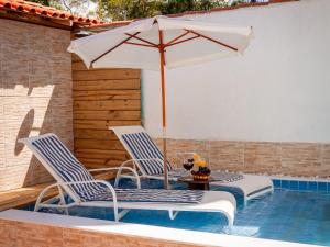 2 sillas y mesa con sombrilla junto a la piscina en Casa Viana Trancoso, en Trancoso