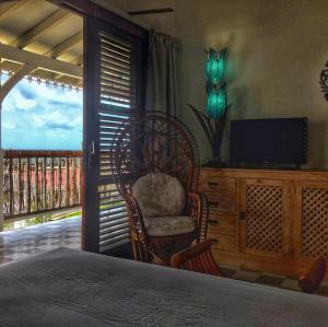 a bedroom with a chair and a television and a balcony at Studio Frangipani dans Villa Fleurs des Iles in Le Vauclin