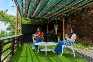 dos mujeres sentadas bajo una pérgola en un césped verde en Cabaña Cielo y Luna en Planes de Renderos