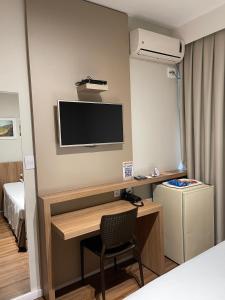 een kamer met een bureau, een televisie en een bed bij Real Hotel in Sete Lagoas