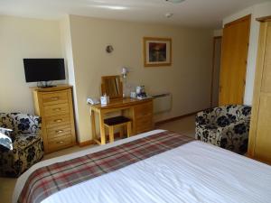 a bedroom with a bed and a desk with a television at The Sands Hotel, Orkney in Burray Village