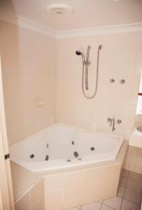 ein weißes Bad mit einer Badewanne und einer Dusche in der Unterkunft The Miners Rest Motel in Kalgoorlie