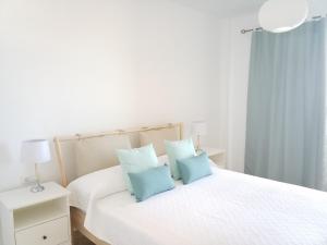 um quarto com uma cama branca e almofadas azuis em Ocean View Playa Negra Apartment em Puerto de Santiago