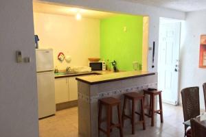 une cuisine avec des murs verts et un comptoir avec des tabourets dans l'établissement Depa Frente al Mar en Acapulco Diamante, à Acapulco