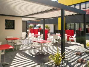 un patio con tavoli e sedie rossi e bianchi di ibis Rennes Beaulieu a Cesson-Sévigné