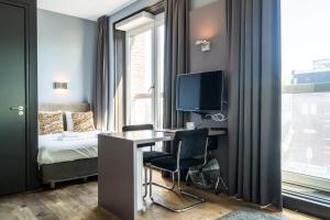 a room with a desk and a bed and a television at Hotel Mosaic Apartments in Amsterdam