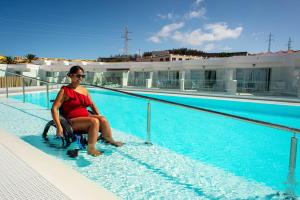 a woman in a wheelchair sitting next to a swimming pool at Hotel Taimar in Costa Calma