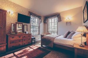 Schlafzimmer mit einem Bett, einer Kommode und Fenstern in der Unterkunft De Courceys Manor Suites & Cottages in Cardiff