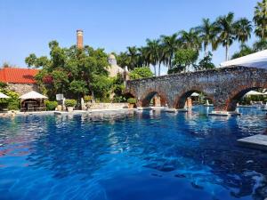 a swimming pool with a stone bridge and palm trees at Hotel Hacienda Vista Hermosa in Tequesquitengo