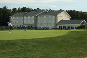 a man playing golf on a golf course with a large building at Crown Pointe Lodge; BW Signature Collection in Farmington