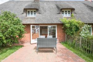 a brick house with a thatched roof with a chair outside at Wellnesswarft Waygaard West in Dagebüll