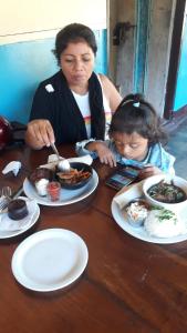 a woman and a child sitting at a table with plates of food at Bananas Guest House Private Room in Altagracia