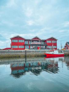 a red building with a red boat in the water at Røst Bryggehotell in Røst