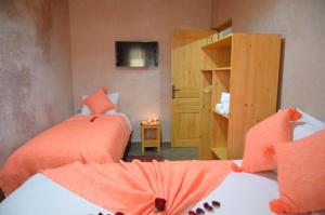 - une chambre avec 2 lits dotés de draps orange et une télévision dans l'établissement Riad Essaouira, à Essaouira