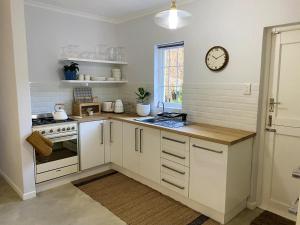 a kitchen with white cabinets and a clock on the wall at Daisy Cottage in Hermanus