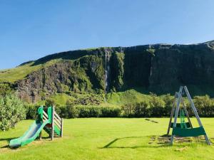 a playground with two slides in a field with a waterfall at Paradise Cave Hostel & Guesthouse in Seljaland