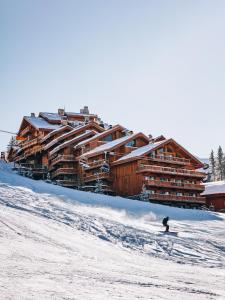 una persona esquiando por una pista cubierta de nieve frente a un lodge en Hotel Le Coucou Méribel en Méribel