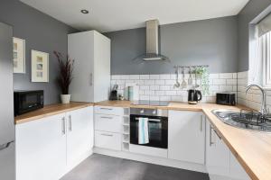 a kitchen with white cabinets and a sink at Links to M62 - 3 bedroom property in Golcar