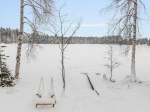 a snow covered field with two benches and trees at Holiday Home Taimisto by Interhome in Juhanala