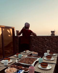 a woman standing on a balcony with a table of food at TOODA House in Imsouane