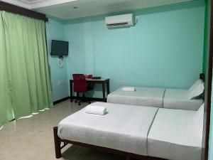 a room with two beds and a desk with a tv at Myoldhouse in Lahad Datu