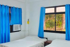 een kamer met 2 bedden en een raam met blauwe gordijnen bij RedDoorz Hostel Hardin De Corales La Union in San Fernando