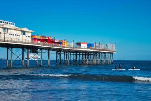 two people on a surfboard in the ocean near a pier at Apartment 5 - 1 Bedroom Sea Front-Sea Views-Free Parking in Paignton