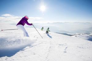 ロデンゴにあるPension Volggerの雪に覆われた坂道を2人がスキーで下りている