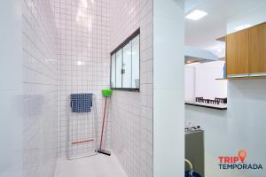 a white tiled bathroom with a red hose at Apartamento com ar condicionado à 100 metros da praia - Edifício Ibiza in Ubatuba +22 photos