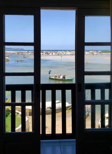 a window view of a beach with a boat in the water at Casa Rio - 04 Quartos de Frente para o Mar in Guarda do Embaú
