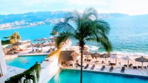 a view of a resort with a palm tree and the ocean at SUITE EN TORRES GEMELAS a pie de playa 1403 N in Acapulco