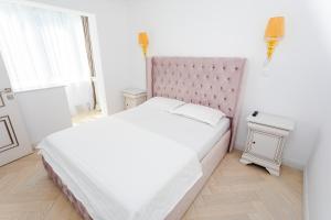 a white bedroom with a large bed with a pink headboard at Apartament Amaya in Bistriţa