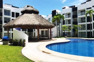 a swimming pool with a straw umbrella next to a building at Hermoso departamento con alberca in Manzanillo +9 photos
