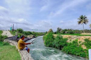 a man is sitting on a stone wall while fishing in a river at Brindavan Garden Resort & Spa in Mysore